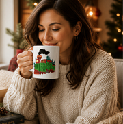 A woman in a white sweater is sitting on a couch, holding a mug with a Christmas-themed design and smiling.