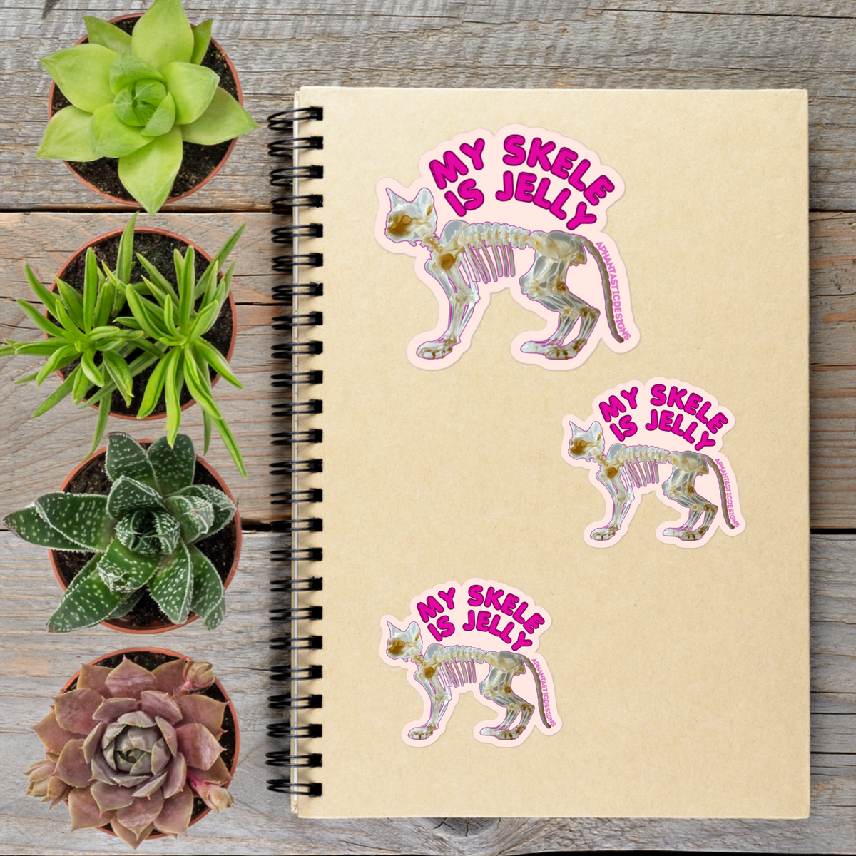 a spiral notebook with stickers on it, surrounded by potted plants.