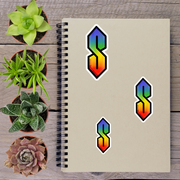 a spiral-bound notebook with three colorful stickers of the letter 'S' on it, along with four potted succulent plants arranged around the notebook.
