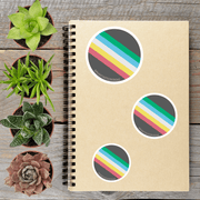 a spiral-bound notebook with three colorful stickers on it, placed on a wooden surface alongside several potted succulent plants.